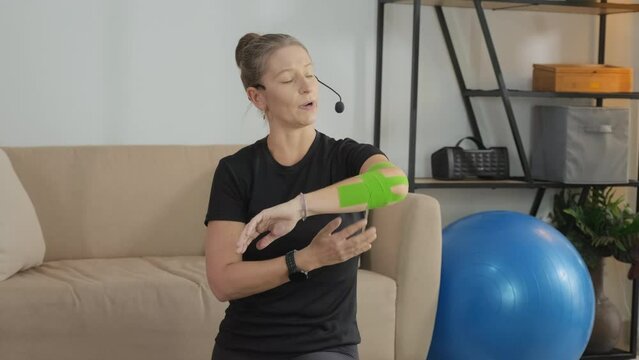 Tilt up shot of female coach explaining how to use tape on elbow while giving online class at home
