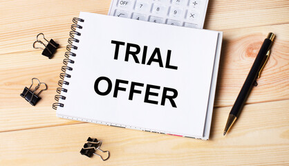 Blank notepad with text TRIAL OFFER, pen, calculator and paper clips on office wooden table.