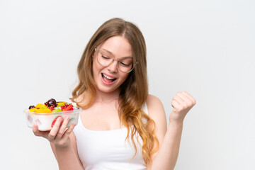 Young pretty woman holding a bowl of fruit isolated on white background celebrating a victory
