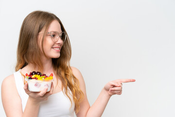 Young pretty woman holding a bowl of fruit isolated on white background pointing to the side to present a product