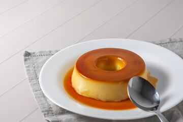 pudim de leite, also known as flan or milk pudding, isolated on white table with grey cloth. bitten slice with a metallic spoon concept of traditional brazilian dessert