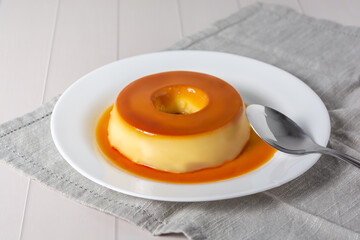pudim de leite, also known as flan or milk pudding, isolated on white table with grey cloth. bitten slice with a metallic spoon concept of traditional brazilian dessert