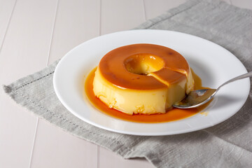 pudim de leite, also known as flan or milk pudding, isolated on white table with grey cloth. bitten...