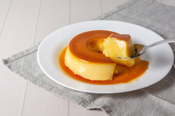 pudim de leite, also known as flan or milk pudding, isolated on white table with grey cloth. bitten...