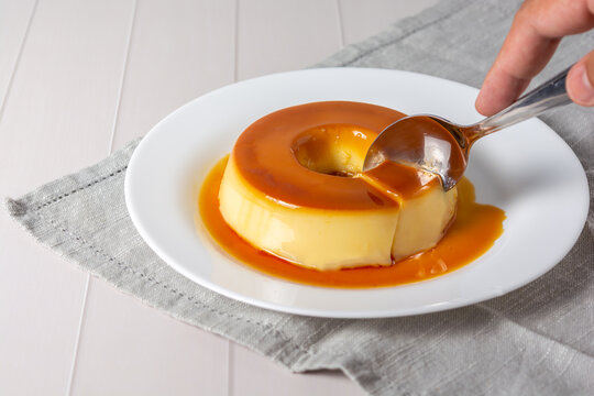 pudim de leite, also known as flan or milk pudding, isolated on white table with grey cloth. bitten slice with a metallic spoon concept of traditional brazilian dessert