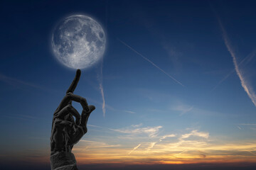 Moon Finger, bronze hand with raised index finger with evening sky in background. On the tip of the...