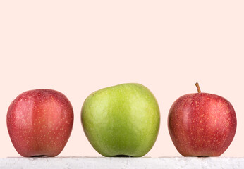 Green and two red ripe apples against a pink background.
