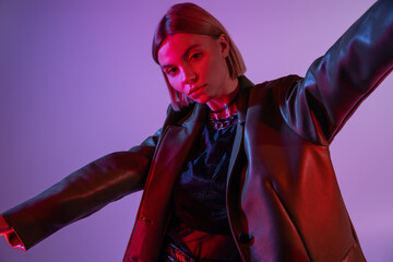 stylish woman in leather jacket posing with outstretched hands isolated on purple.