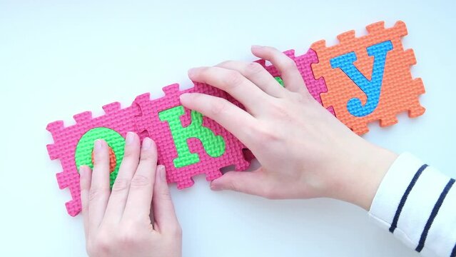 A hand collects a word Okay on a white background from colorful children's soft puzzles. High quality FullHD footage with slow motion
