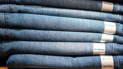 Folded blue jean trousers which are stacked on the selling shelf at clothing store. Object close-up for background photo.