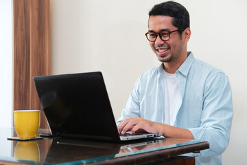 Adult Asian man smiling happy while typing on his laptop