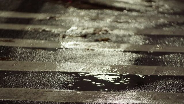 Pedestrian walk and raindrops falling on the aspalt forming a puddle. Heavy rain in city, wet asphalt, rain drops are splashing on the puddle surface. Night