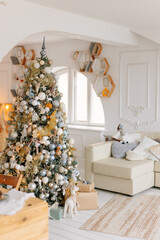 Christmas living room. Fir tree decorated with white and golden toys. Preparations for family dinner, waiting for guests. beige golden background. Simple home interior