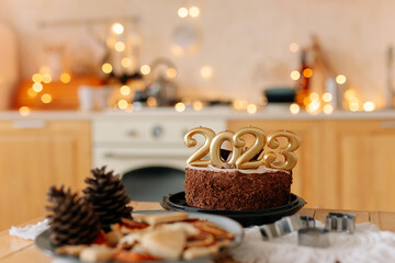 a cake with 2023 candles in Christmas Kitchen. Preparations for family dinner, home recipes, cooking chocolate cake. beige golden bokeh background