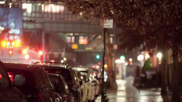 Rainy evening. View of a row of cars parked along the road, blurred street and blinking traffic lights under heavy rain. Raindrops are falling from the sky on the city at night