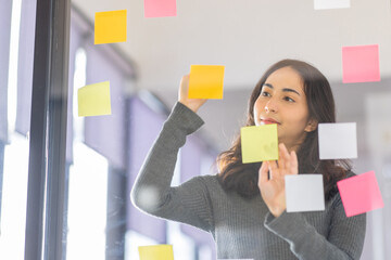 Business female employee with many conflicting priorities arranging sticky notes commenting and brainstorming on work priorities colleague in a modern office.