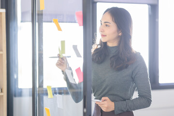 Business female employee with many conflicting priorities arranging sticky notes commenting and brainstorming on work priorities colleague in a modern co-working space.