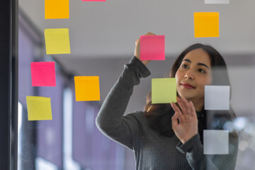 Business female employee with many conflicting priorities arranging sticky notes commenting and brainstorming on work priorities colleague in a modern office.