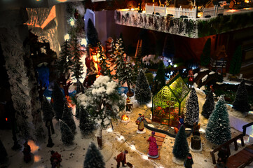 Christmas village with a flower greenhouse in the mountains with old-fashioned dressed figurines, a campfire and snowy fir trees