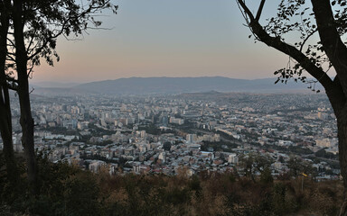 View of Tbilisi City from the mountain, Mtatsminda park, on the sunset throw the trees