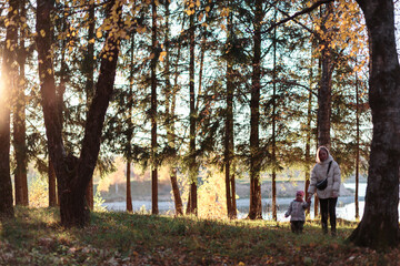Autumn forest at sunset, mother and girl are standing by a tree.