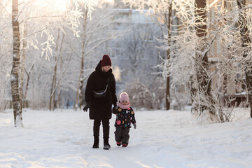 Fototapeta na wymiar Mom and daughter are walking in the snow on a clear sunny frosty day.