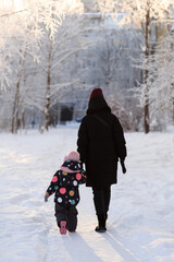 Fototapeta na wymiar Mom and daughter are walking in the snow on a clear sunny frosty day. Vertical Orientation