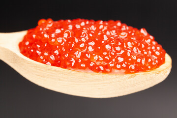 Delicious red caviar in wooden spoon on black background
