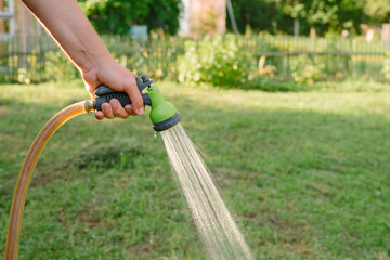 Gardeners hand holds a hose with a sprayer and watered the lawn in country house