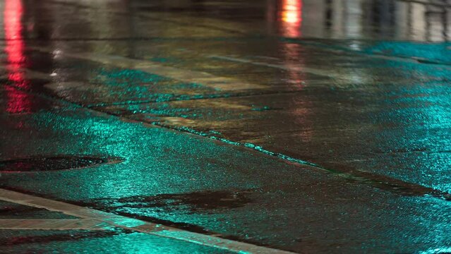 Road and raindrops falling on the aspalt forming puddles. Cars are driving along the wet road. Heavy rain in city, wet asphalt, rain drops are splashing on the puddles surface. Night
