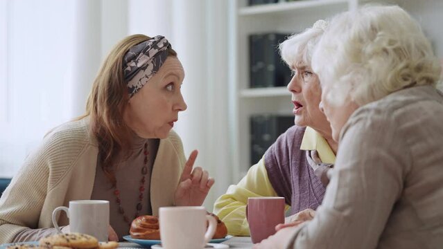 Three senior women gossiping while drinking tea, discussing latest news, secrets