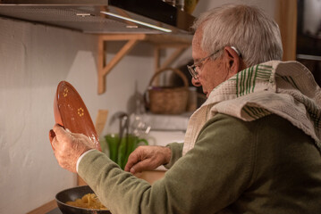 retired senior man cooking potato omelette, rustic kitchen