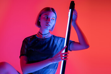 young and trendy woman posing in blue light of neon lamp on coral and pink background.