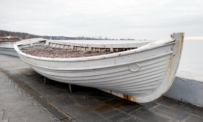 Naklejka premium old rusty wooden white boat on a concrete pier at sunset