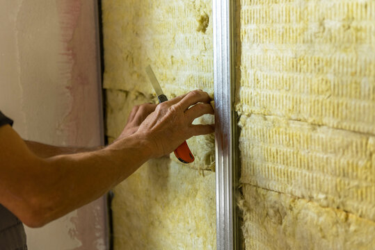 Worker insulating a room wall with mineral rock wool thermal insulation.