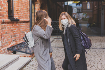 Young pretty girls friends in medical masks having fun outdoor in autumn evening in city laughing and going crazy - end of pandemic concept