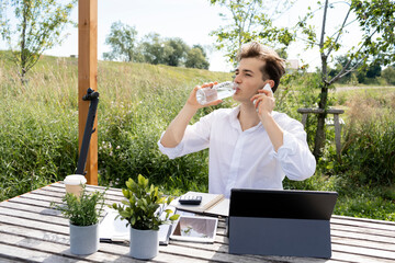 Fototapeta premium young attractive man working or studying in park and sitting by wooden table