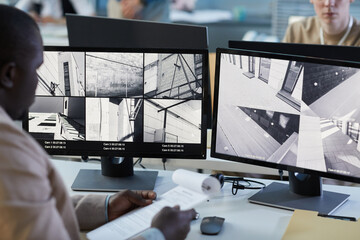 Background image of man looking at surveillance camera feeds at computer screens in security and...