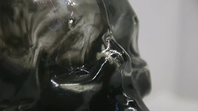 Black Paint floats inside a glass skull with bubbles close-up on a white background	
