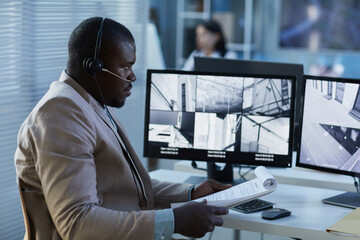 Side view portrait of black man wearing headset while watching surveillance feed on screen in...