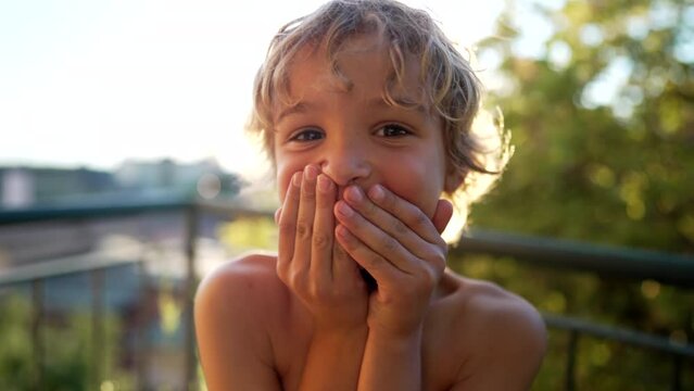 Bashful Little boy kid shocked covering mouth with hands for mistake standing outdoors. secret concept