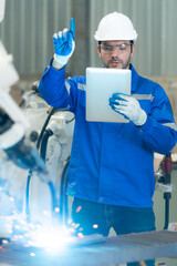 Young male engineers are manipulating a welding robot hand. By combining welding manipulation with...