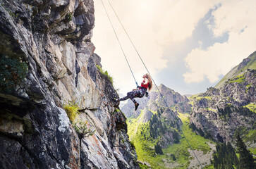 Woman athlete climbing on the high rock in the mountains
