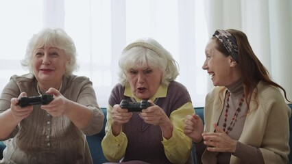 Funny grandmas playing video game with joysticks, celebrating victory, hobby