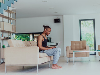 African American sport man in glasses sitting at a table in a modern living room, using a laptop for business video chat, conversation with friends and entertainment