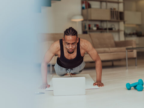 Young African American man working push-ups in the living room while watching online training on laptop
