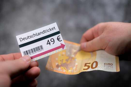 Hands holding 49-Euro-Ticket mockup and 50 euro cash bill against out of focus gray background with barcode and minimal design elements on the ticket visible