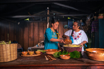 Retrato de dos mujeres indigenas preparando masa de elotes para acer tamales, tascales, atole y tortillas. 