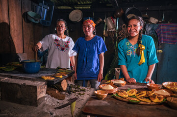 Mujeres indigenas preparando alimentos de maìs, atole, tamalitos y "Tascales" tipo de tortillas de elote sobre una hoja de una flor llamada hortencia en una estufa de leña. 