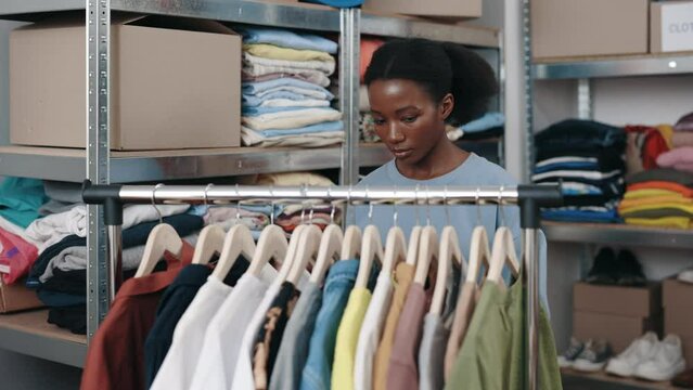 Multiracial brunette woman working with clothes for recycle while working at the second hand or charity shop. Reuse, second-hand, conscious consumer, sustainability concept
